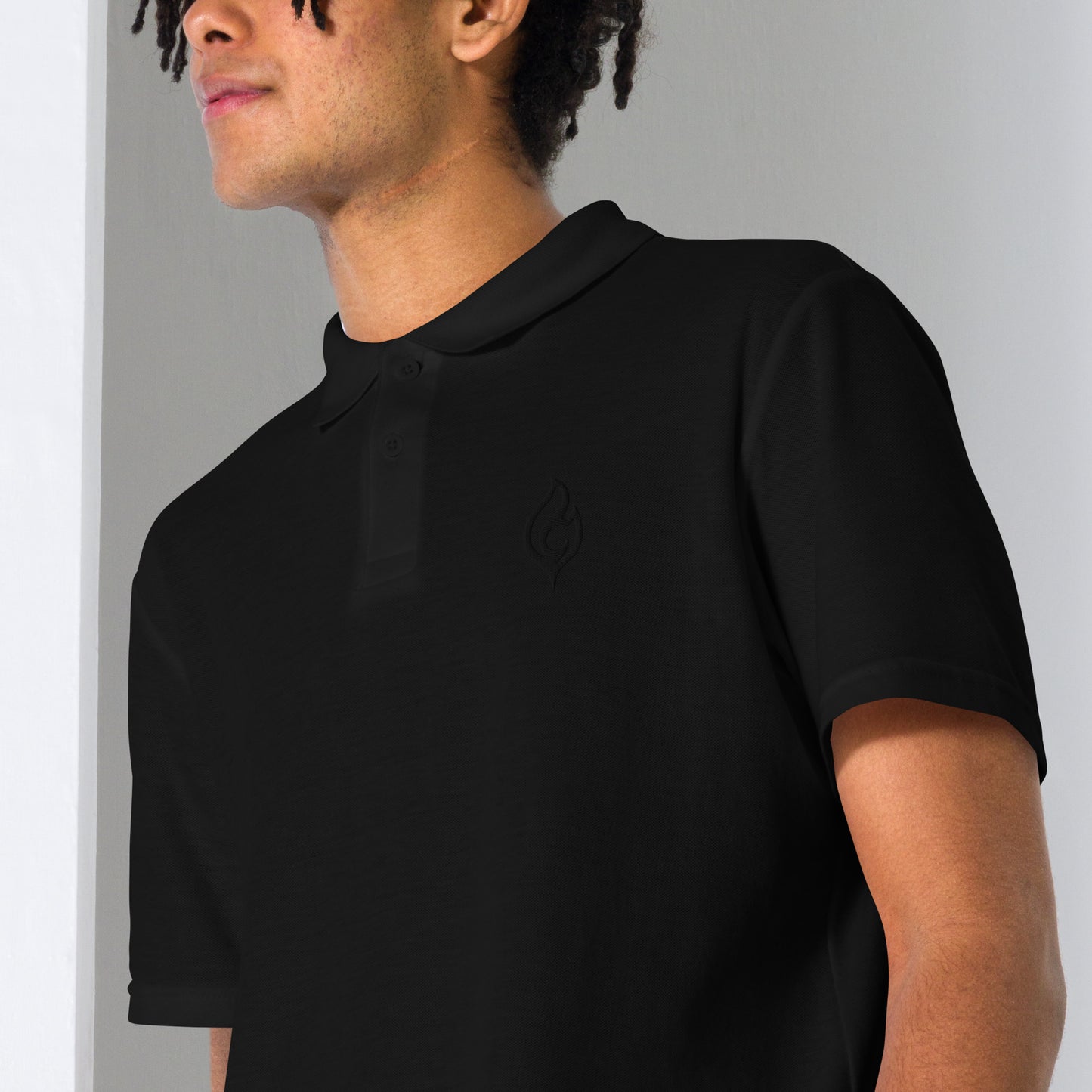 Male model close-up angled pose wearing Ciao Cult Tonal Black-on-Black Signature Flame Polo, subtle embroidered flame detail visible.
